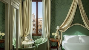 Ein Zimmer mit einem Bett, einem Tisch, Stühlen und einem Fenster mit Vorhängen sowie Blick auf Gebäude.