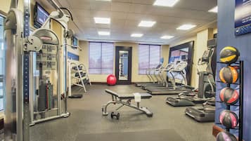 Une salle de sport équipée de tapis de course, de vélos elliptiques, d’un banc de musculation et de différents ballons d’exercice.