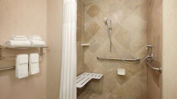 A shower area with a grab bar, a towel rack with folded towels, and a showerhead.