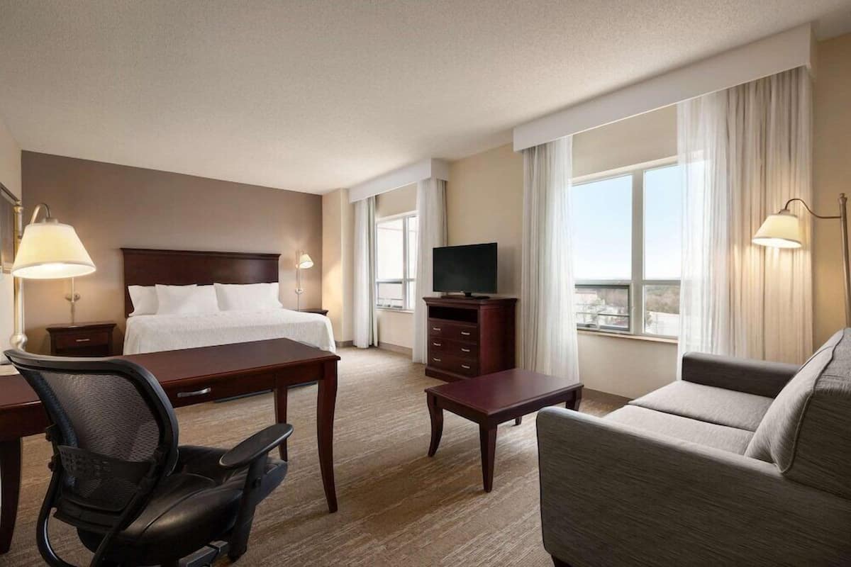 A hotel room with a bed, desk, chair, television, and a sofa.