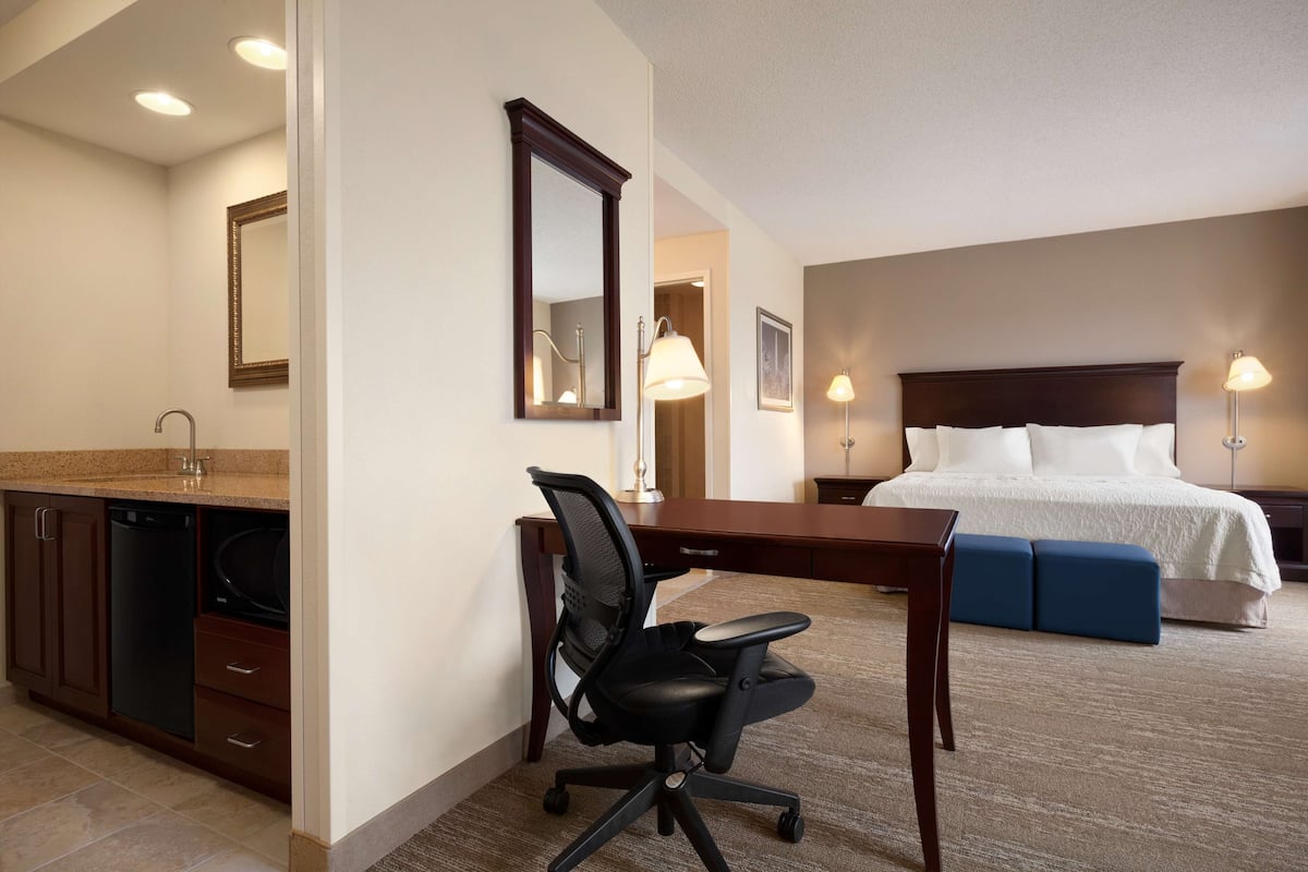 A hotel room with a desk, chair, bed, and a bathroom with a sink and mirror.
