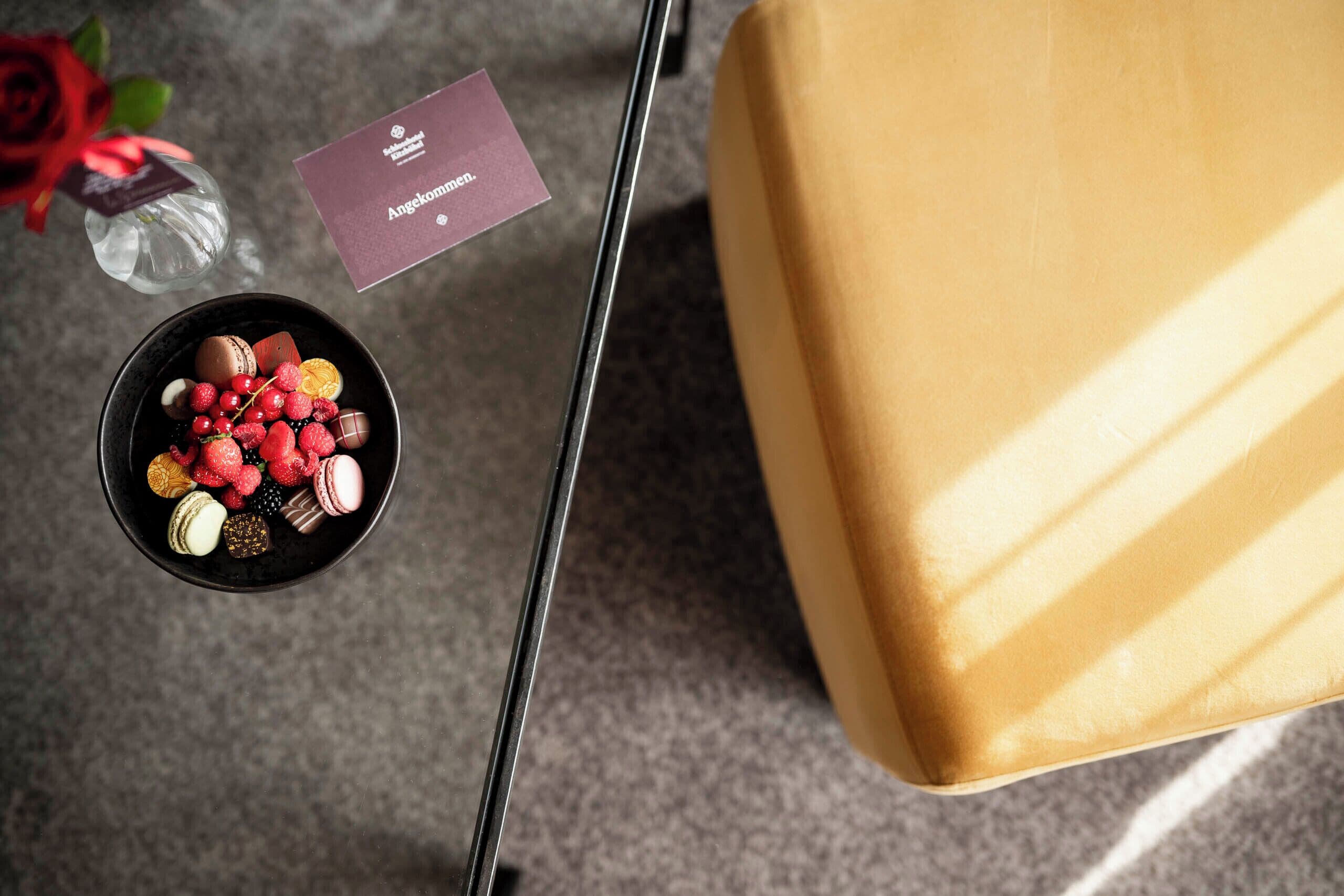 A table with a bowl of assorted pastries, a small card, and a glass with a rose.