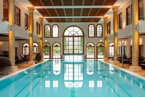 A large indoor swimming pool with multiple arched windows and columns.