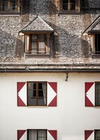 A multi-story building with a shingled roof and multiple windows with red and white shutters.