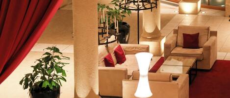 A lobby with a red curtain, a potted plant, a candelabra, and several sofas with red cushions.