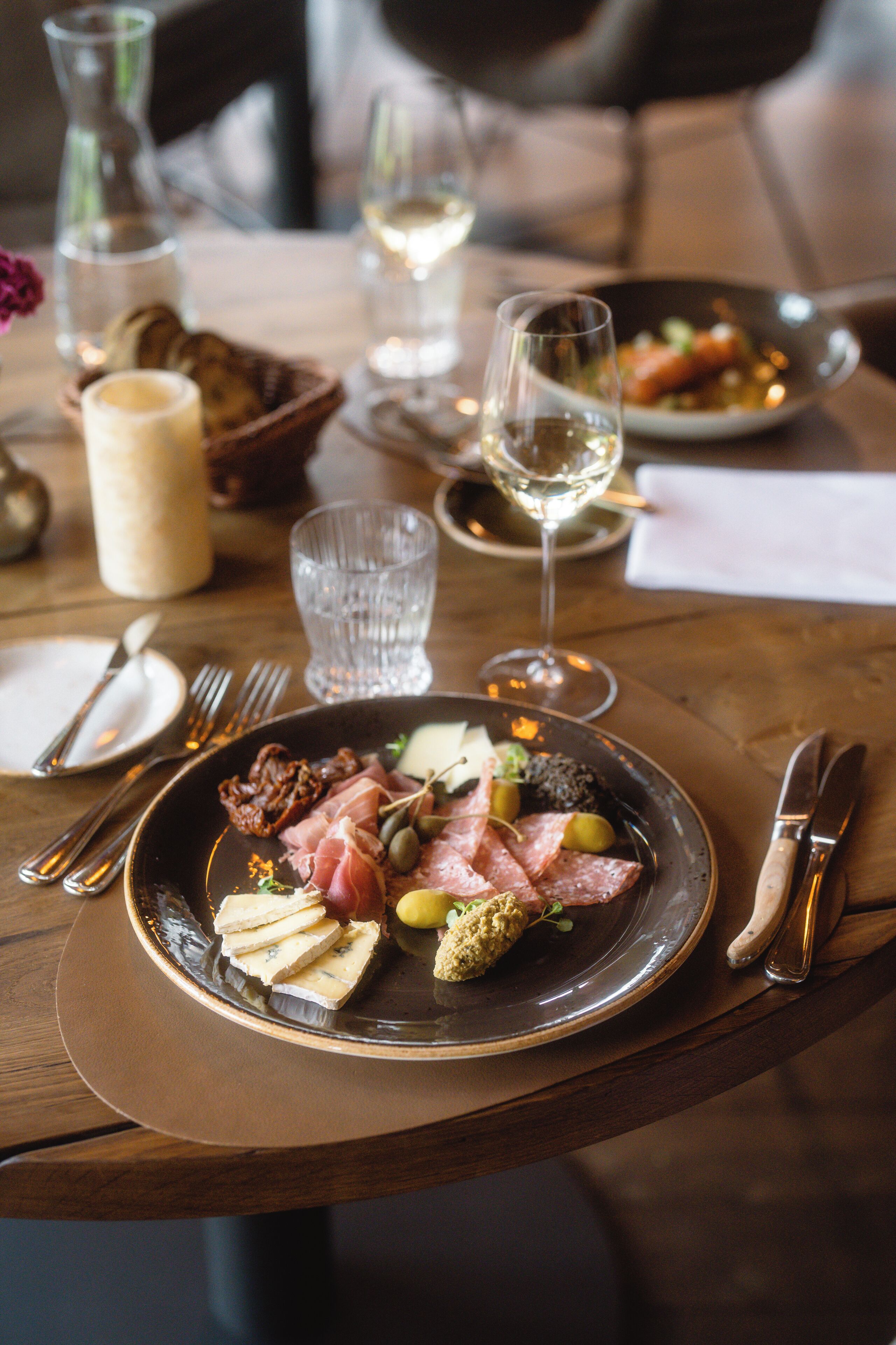 A dining table with plates of food, cutlery, and glasses of wine.