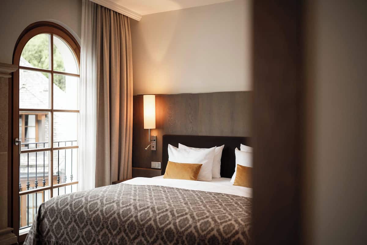 Ein Hotelzimmer mit einem großen Bett, einem Nachttisch mit Lampe und einem Fenster mit Vorhängen.