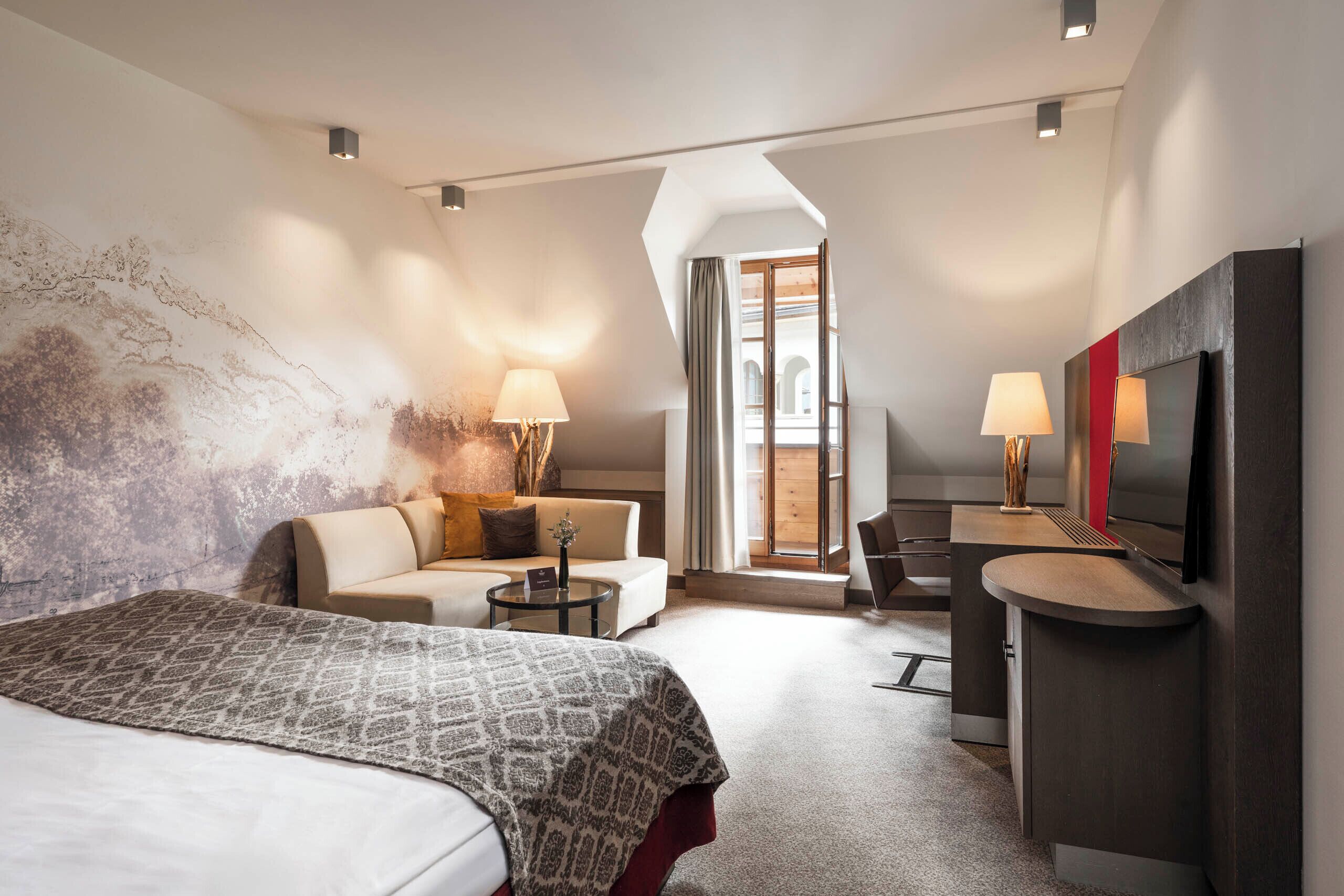 A modern hotel room with a large bed, a sofa, a desk, and a TV.