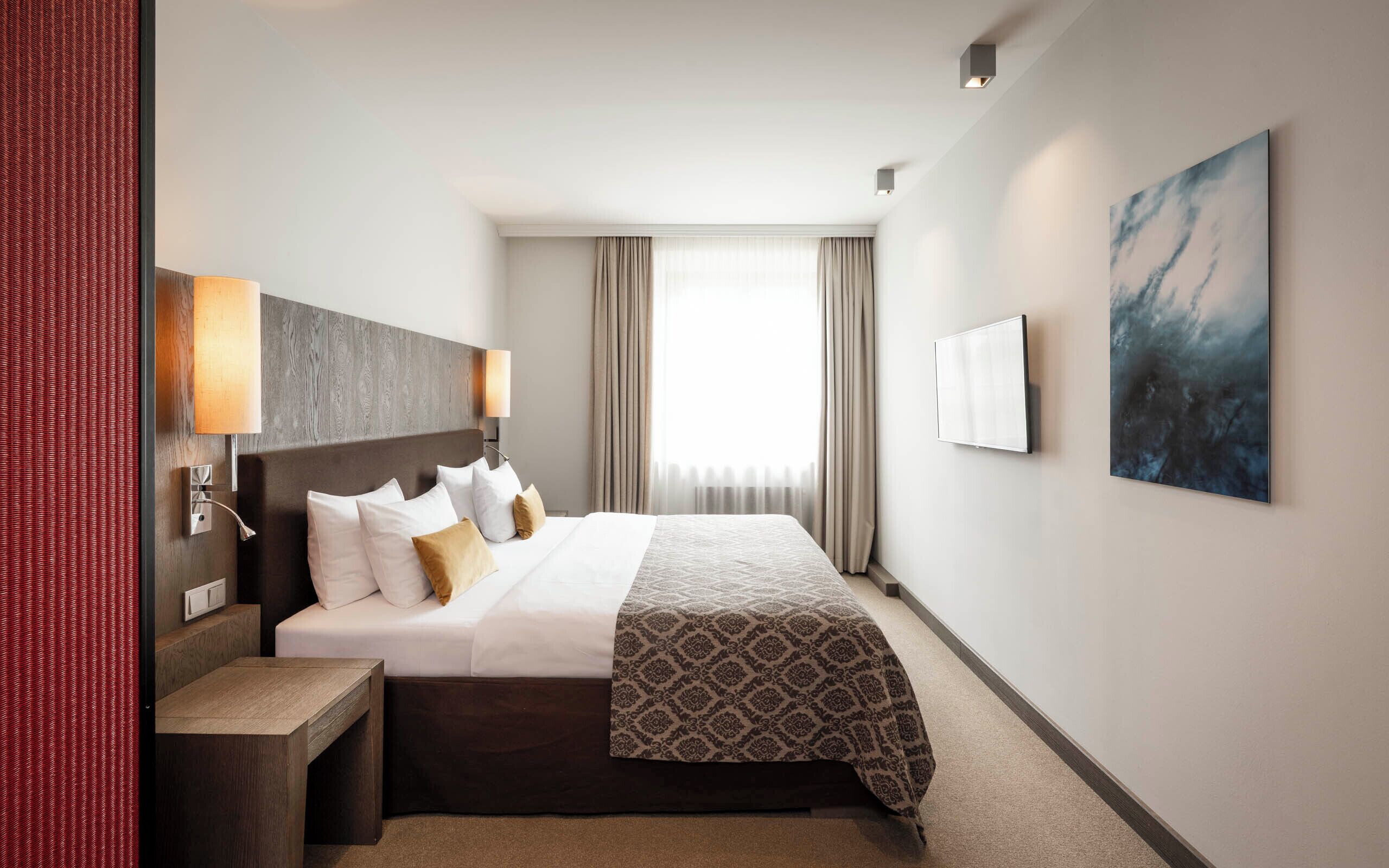 A hotel room with a large bed, bedside lamps, a flat-screen TV, a painting, and a view of the outdoors.