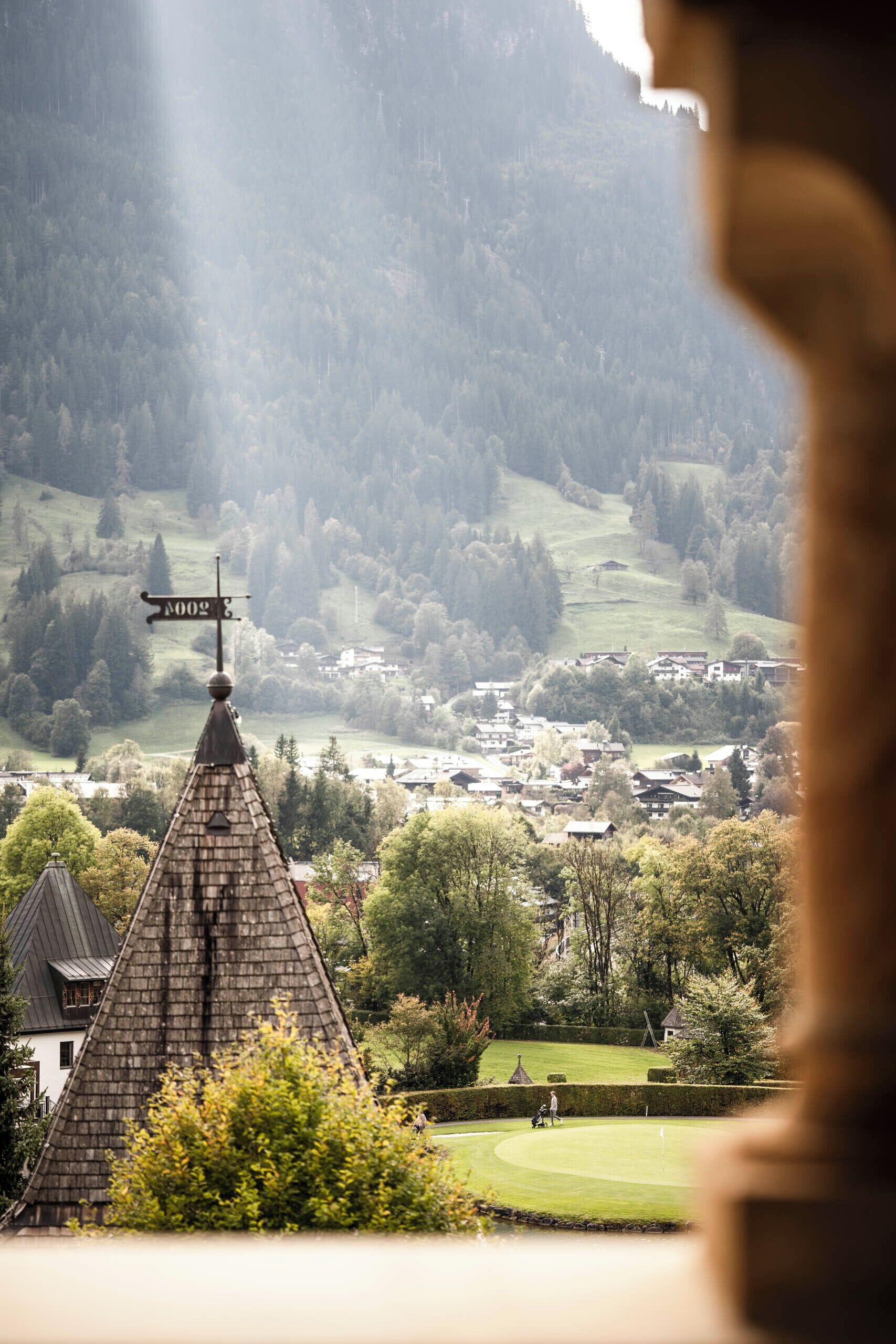 Vista de un pueblo con un campanario de iglesia destacado, un campo de golf y zonas verdes circundantes.