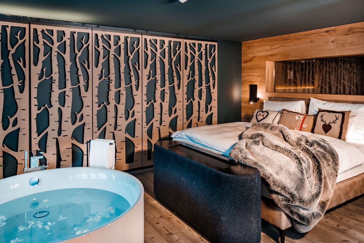 Ein modernes Schlafzimmer mit einem großen Bett, einem Holzkopfteil, einer integrierten Badewanne und einer dekorativen Wandverkleidung.