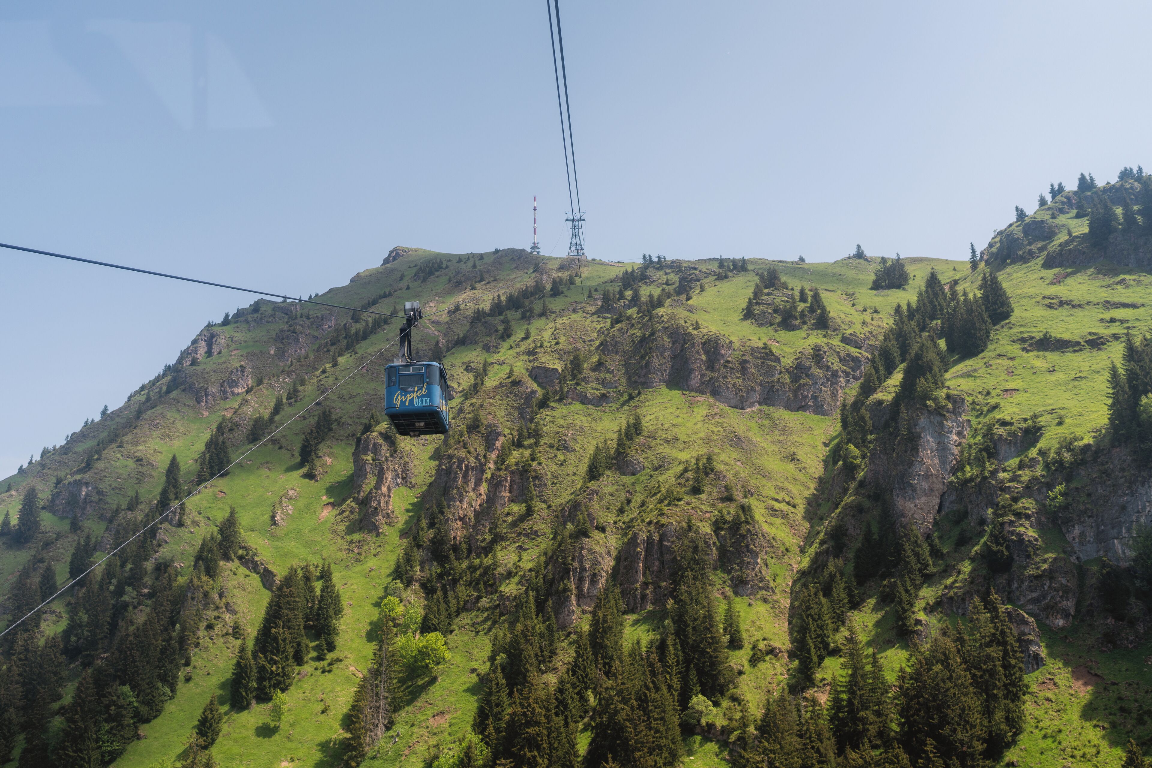 Un teleférico asciende una montaña empinada, verde, con afloramientos rocosos y densos bosques.