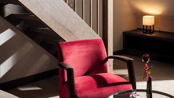 A modern living room with a red armchair, a glass coffee table, and a staircase with a wooden railing.