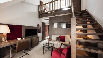 A modern living room with a TV, sofa, and red chair. A staircase leads to an upper level.