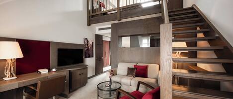 A modern living room with a TV, sofa, and red chair. A staircase leads to an upper level.