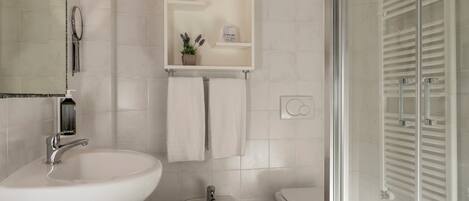 Une salle de bain avec un lavabo blanc, un bidet, des toilettes et une douche à parois de verre.