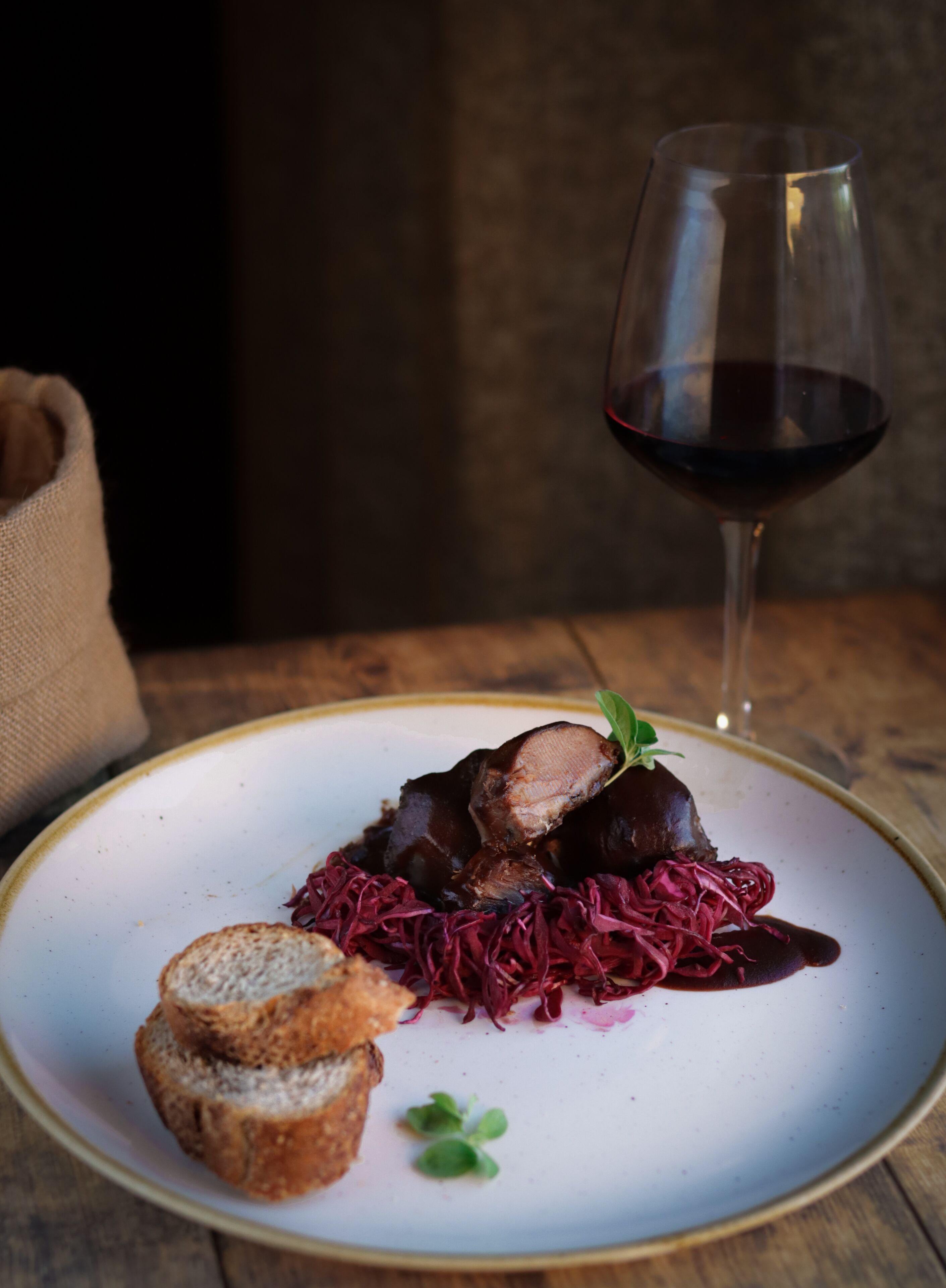 A plate of food with bread and a glass of red wine on a wooden table.