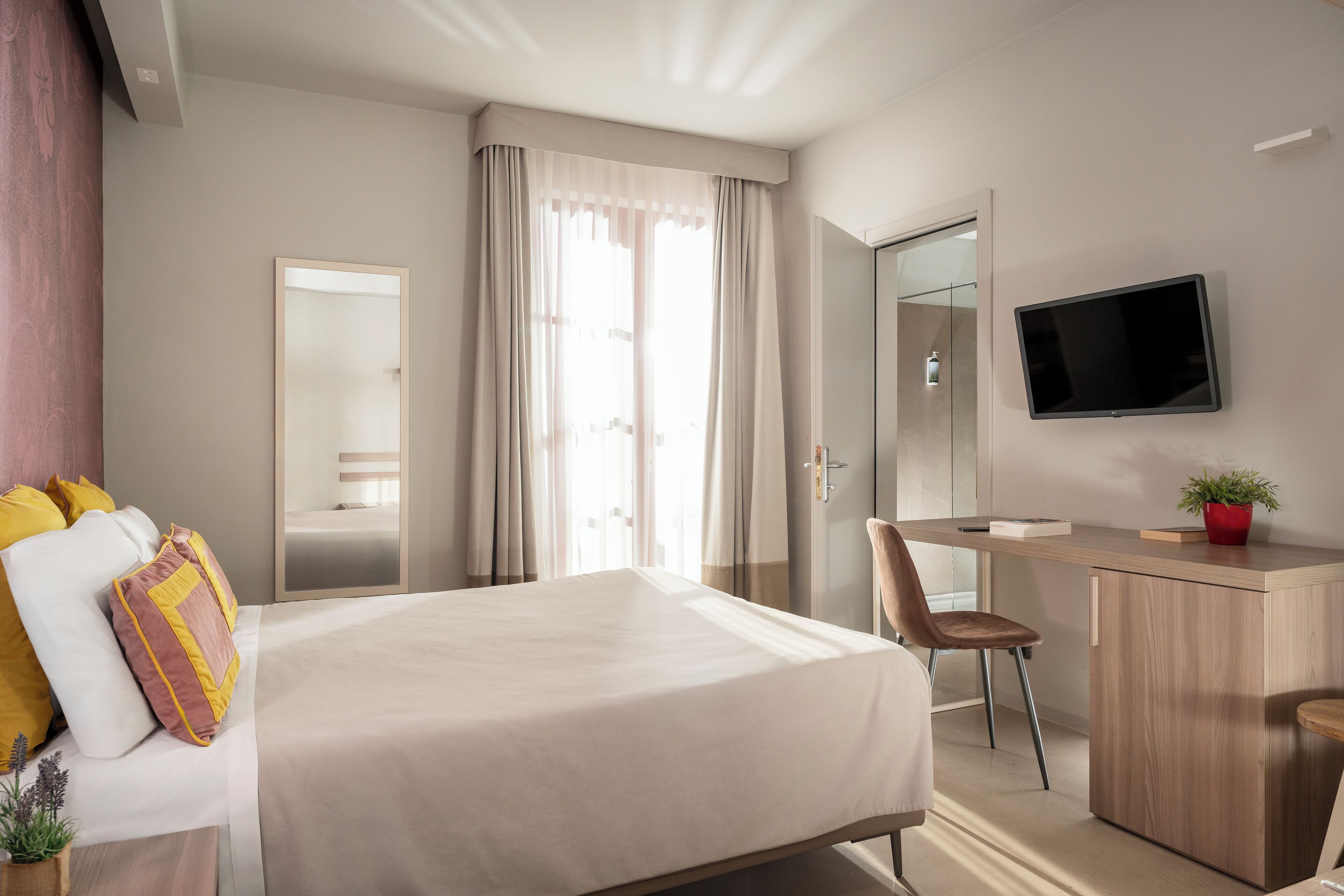 Habitación de hotel con cama, escritorio, silla, televisor y espejo.