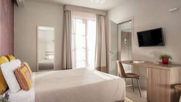 A hotel room with a bed, a desk, a chair, a TV, and a mirror.