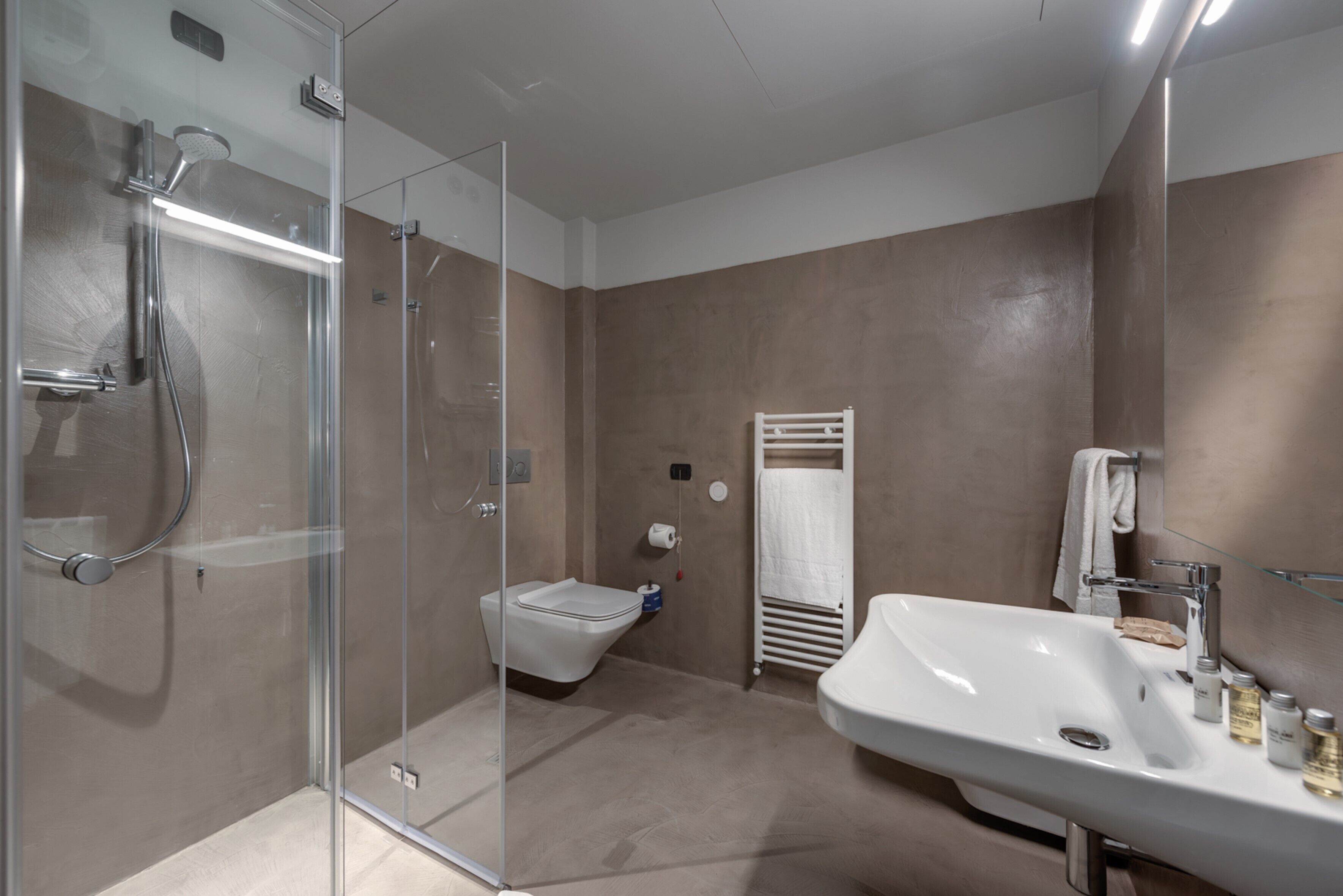 Un baño moderno con ducha envuelta en vidrio, un inodoro y un lavamanos amplio con artículos de aseo.