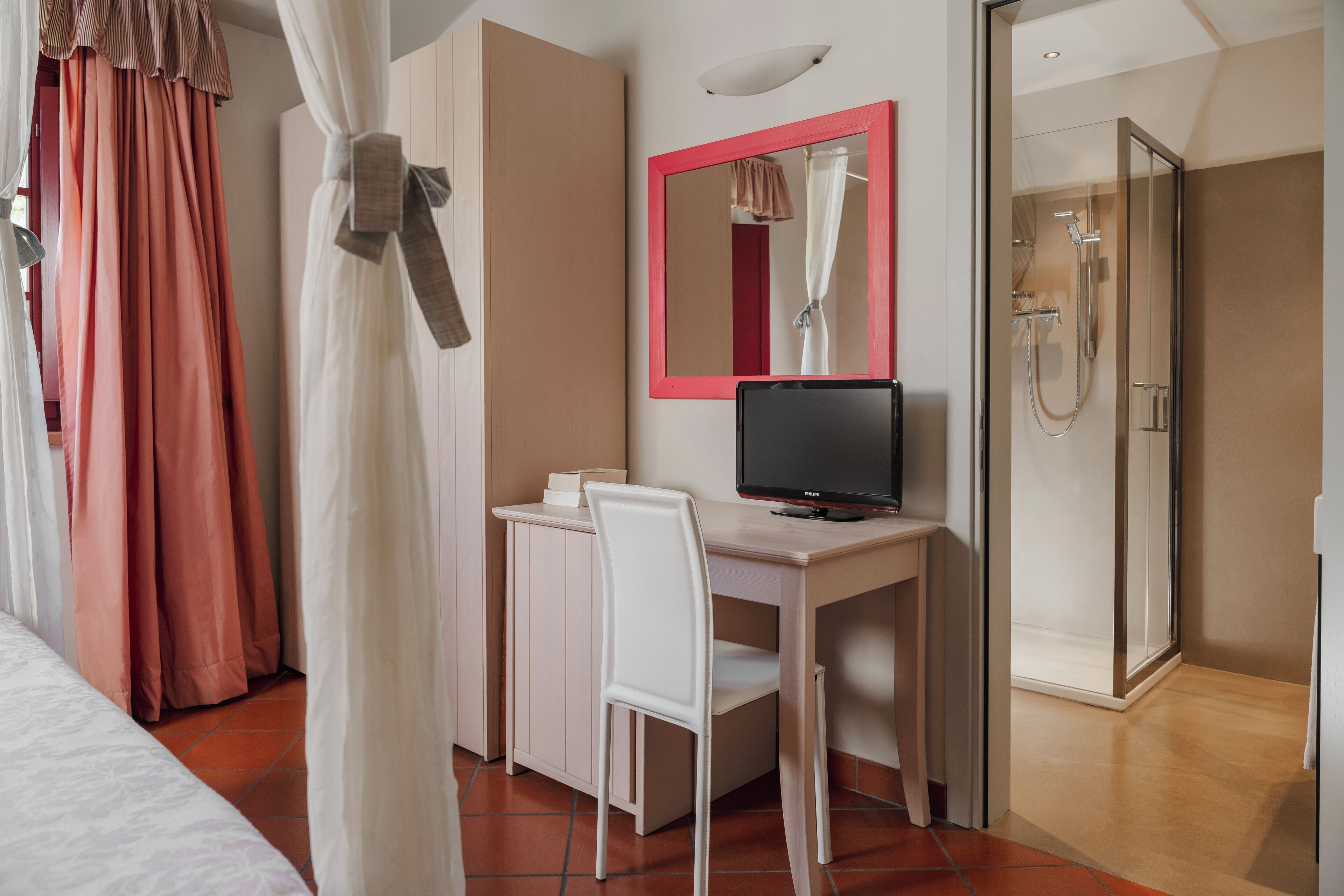 A hotel room with a bed, a desk with a computer, a shower, and a mirror.