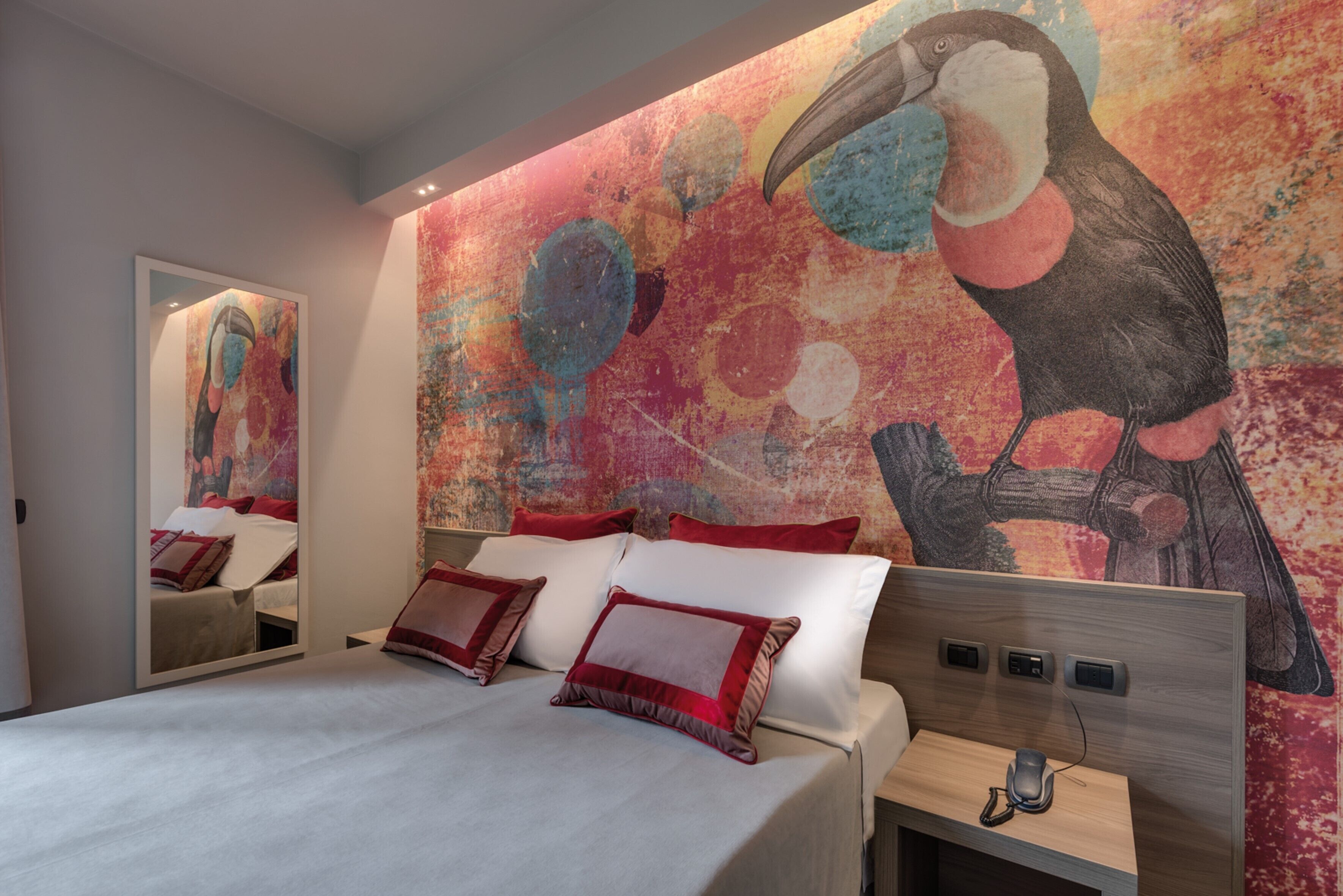 A modern hotel room with a large bed, a nightstand, and a wall mural of a toucan.