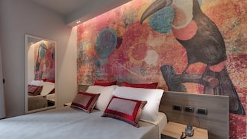 A modern hotel room with a large bed, a nightstand, and a wall mural of a toucan.