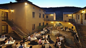 An outdoor dining area with multiple tables and chairs, surrounded by buildings with balconies and a staircase.
