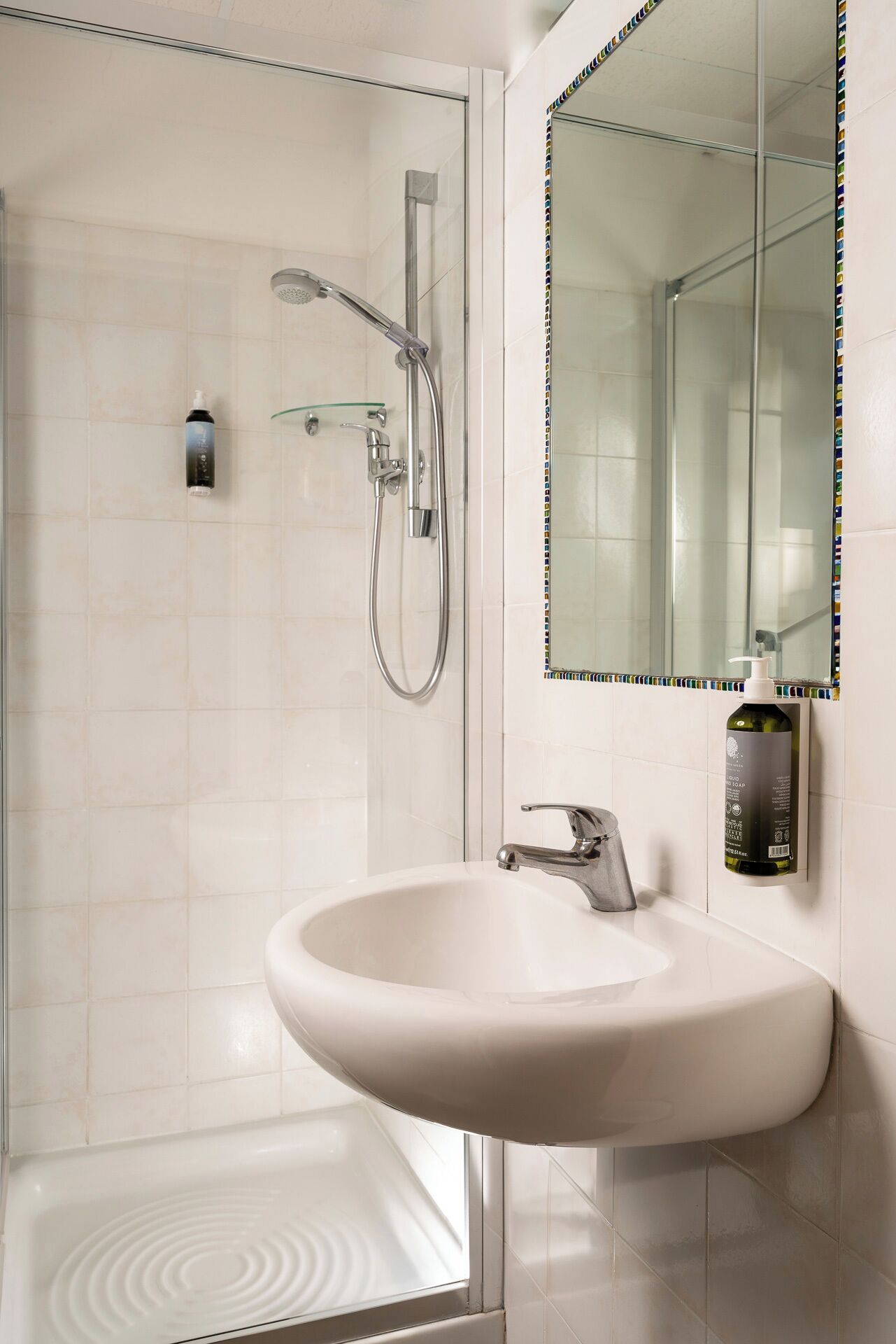 A modern bathroom with a white sink, a glass shower enclosure, and a large mirror with a colorful border.