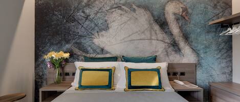 A bedroom with a large bed, two nightstands, a vase of flowers, and a wall mural of swans.