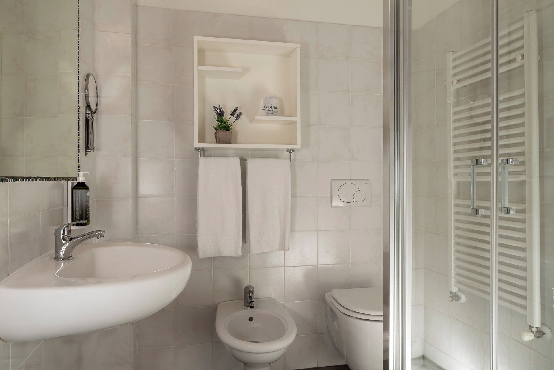 Een badkamer met een wit wastafel, bidet en toilet, een spiegel en een handdoekhouder.