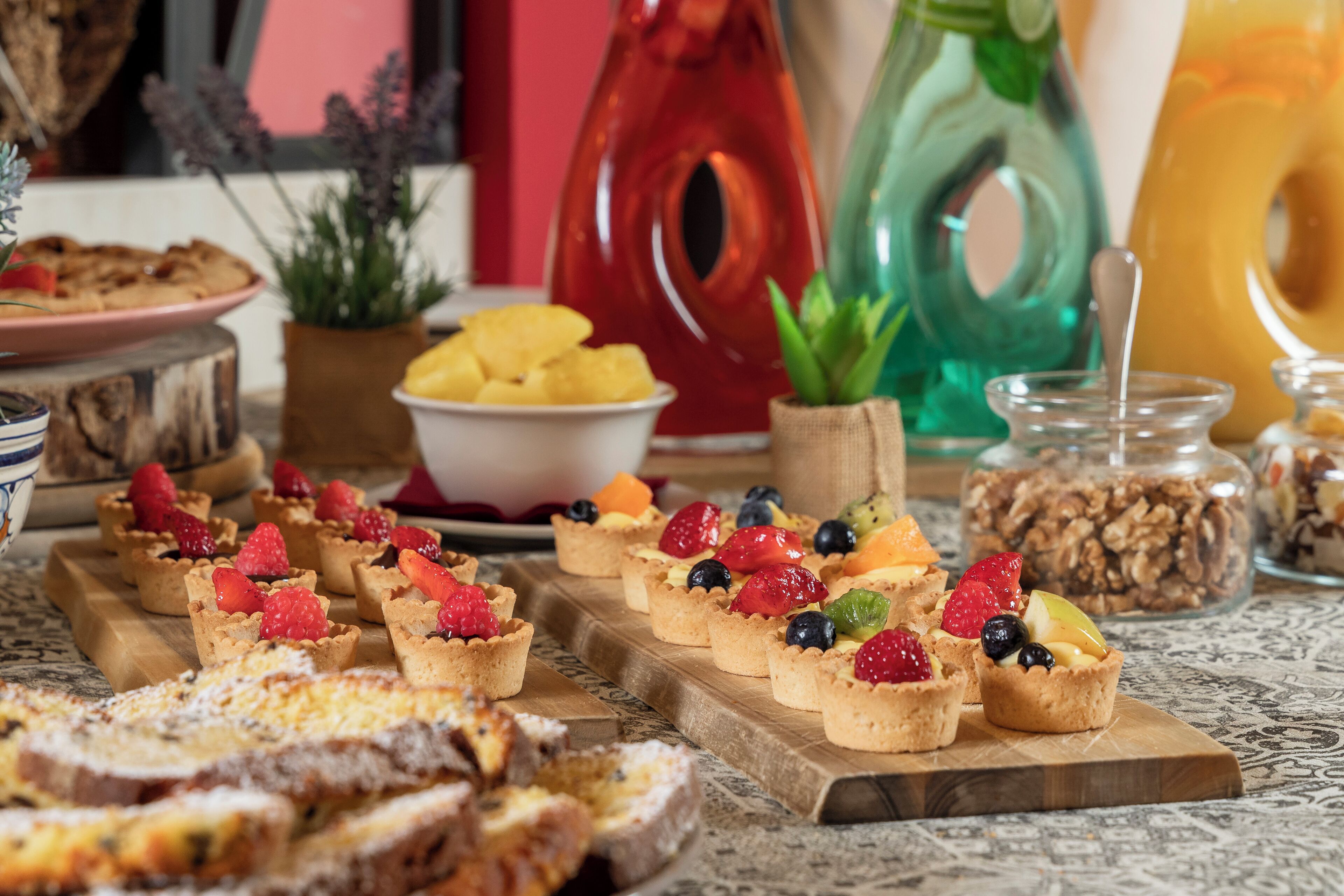 Une table sur laquelle on trouve divers aliments, notamment des tartes aux fruits, un saladier rempli de fruits et un bocal de granola.