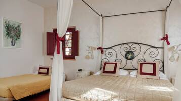 A bedroom with a four-poster bed, a smaller bed, a nightstand, and a wall-mounted lamp.