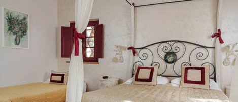 A bedroom with a four-poster bed, a smaller bed, a nightstand, and a wall-mounted lamp.