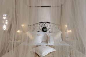 A bed with white linens and a canopy, a round bedside table, and a wall-mounted light fixture. - Hotel Casolare Le Terre Rosse (San Gimignano)