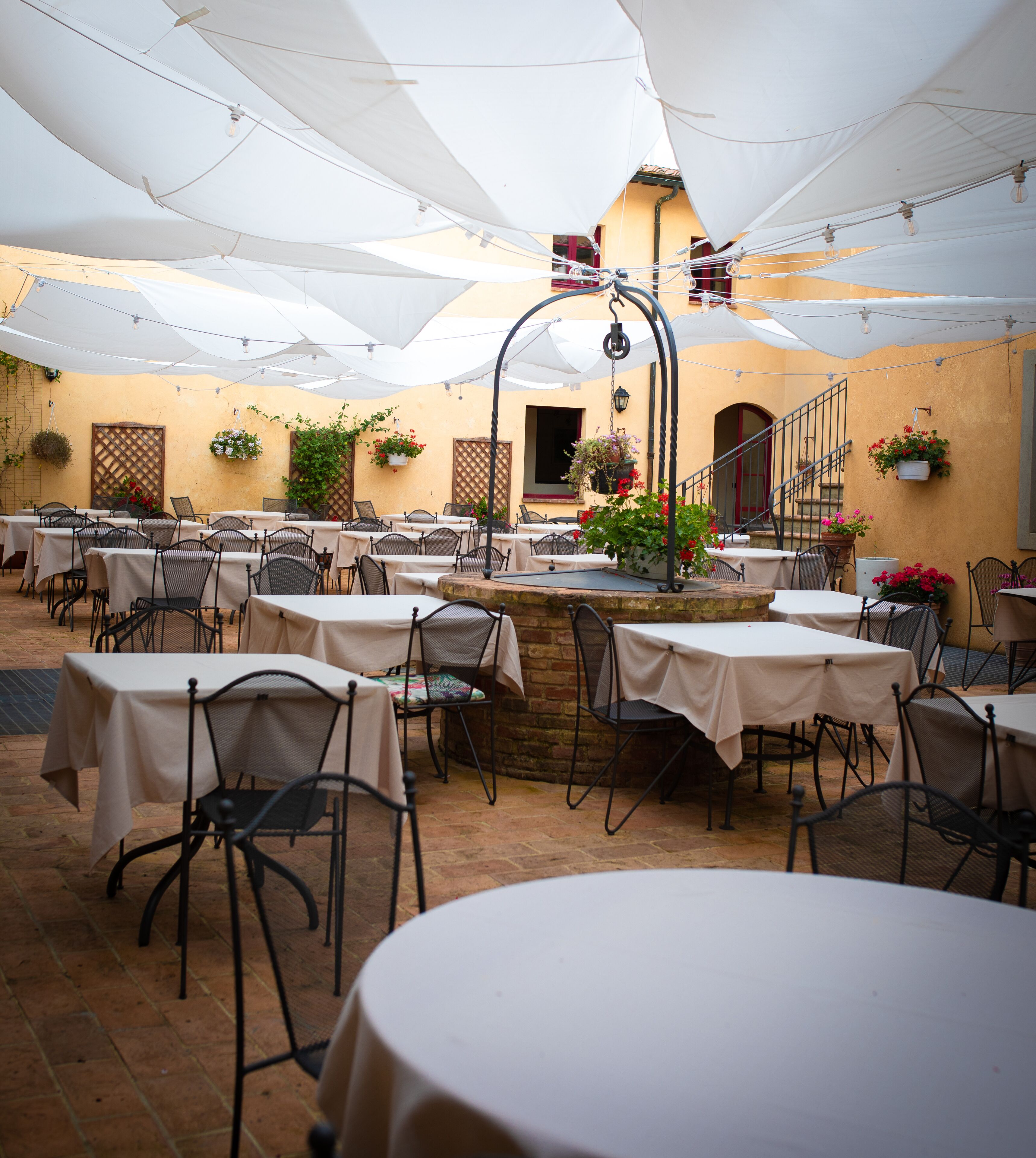 An outdoor dining area with round tables and chairs, covered by white canopies, and surrounded by potted plants.