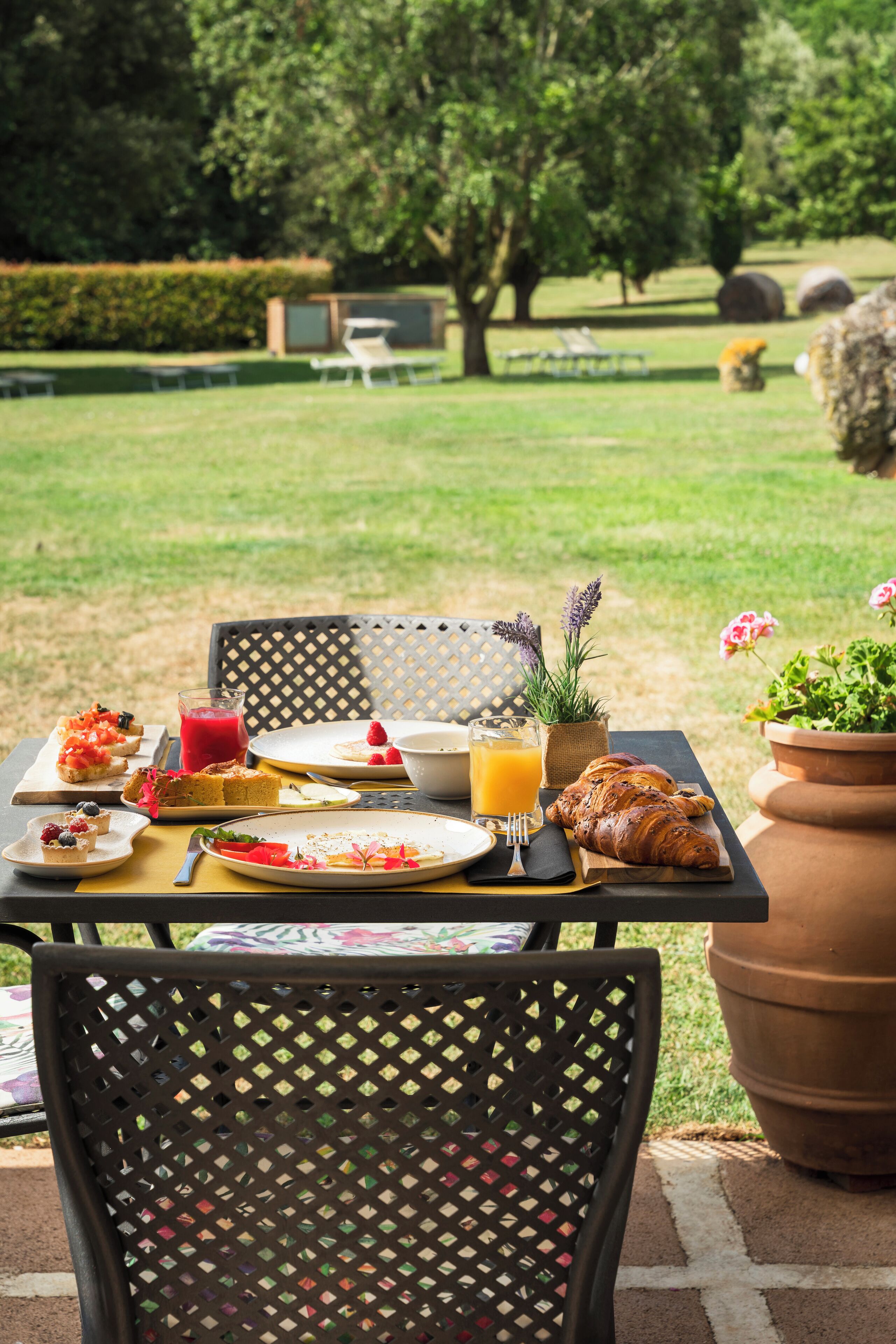 An outdoor dining area with a table set for breakfast, including croissants, fruit, and a glass of orange juice.