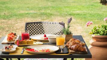 An outdoor dining area with a table set for breakfast, including croissants, fruit, and a glass of orange juice.