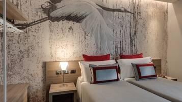 A hotel room with a large mural of an angel on the wall, a wooden headboard, a bedside table with a lamp, and a bed with red and white bedding.