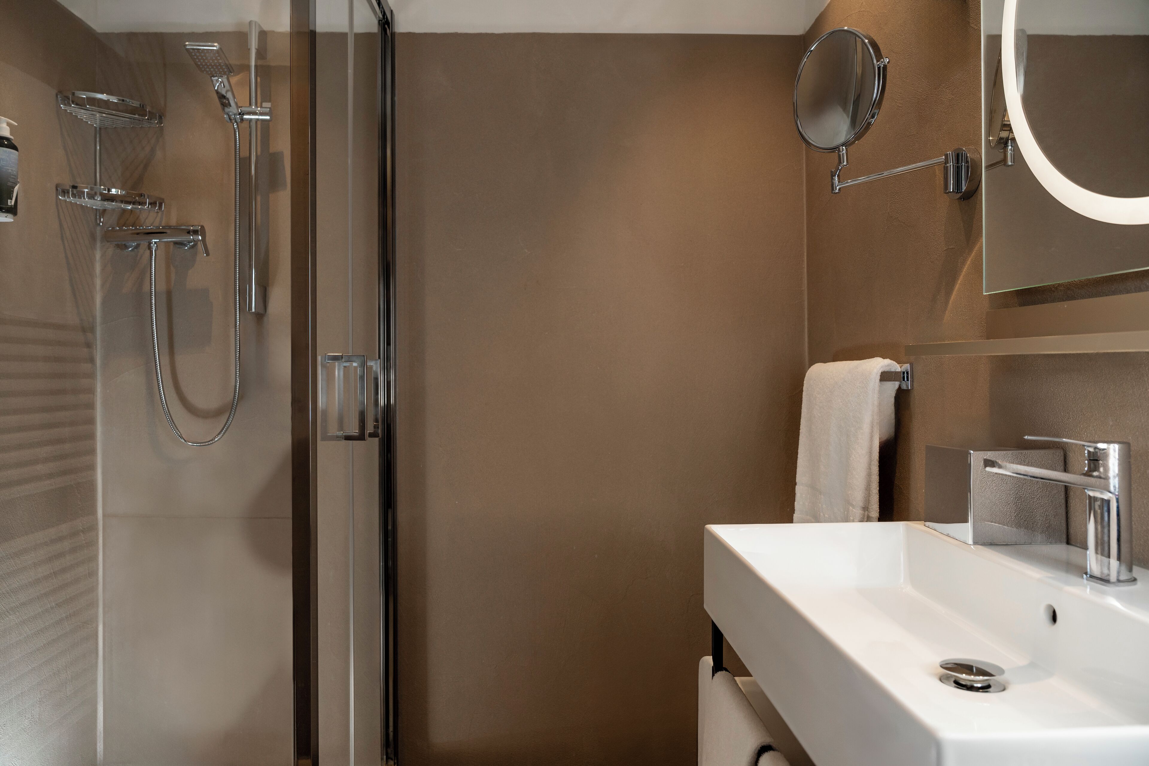 Un baño moderno con ducha envuelta en vidrio, un lavamanos blanco y un espejo con marco redondo.