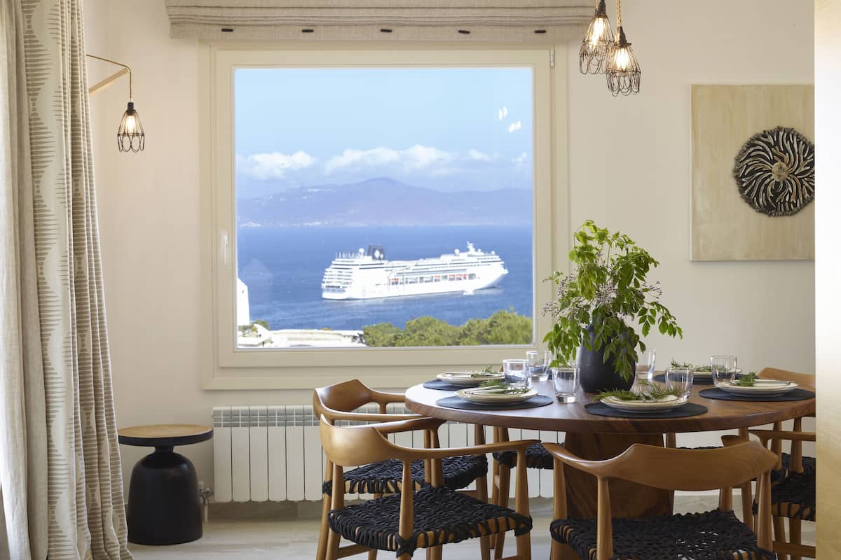 Een eetgedeelte met uitzicht op een cruiseschip, houten stoelen, een ronde tafel en een potplant.