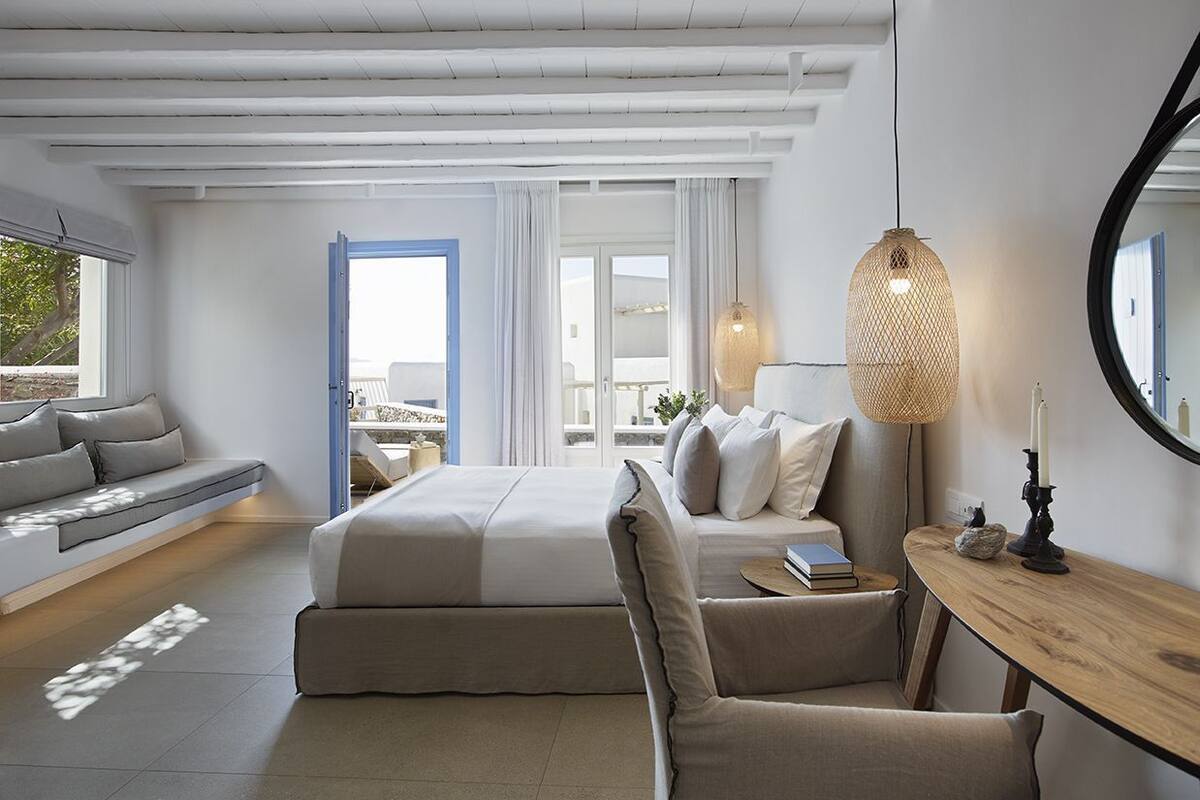 Een moderne slaapkamer met een bed, een zithoek, een houten bijzettafeltje en een grote spiegel.
