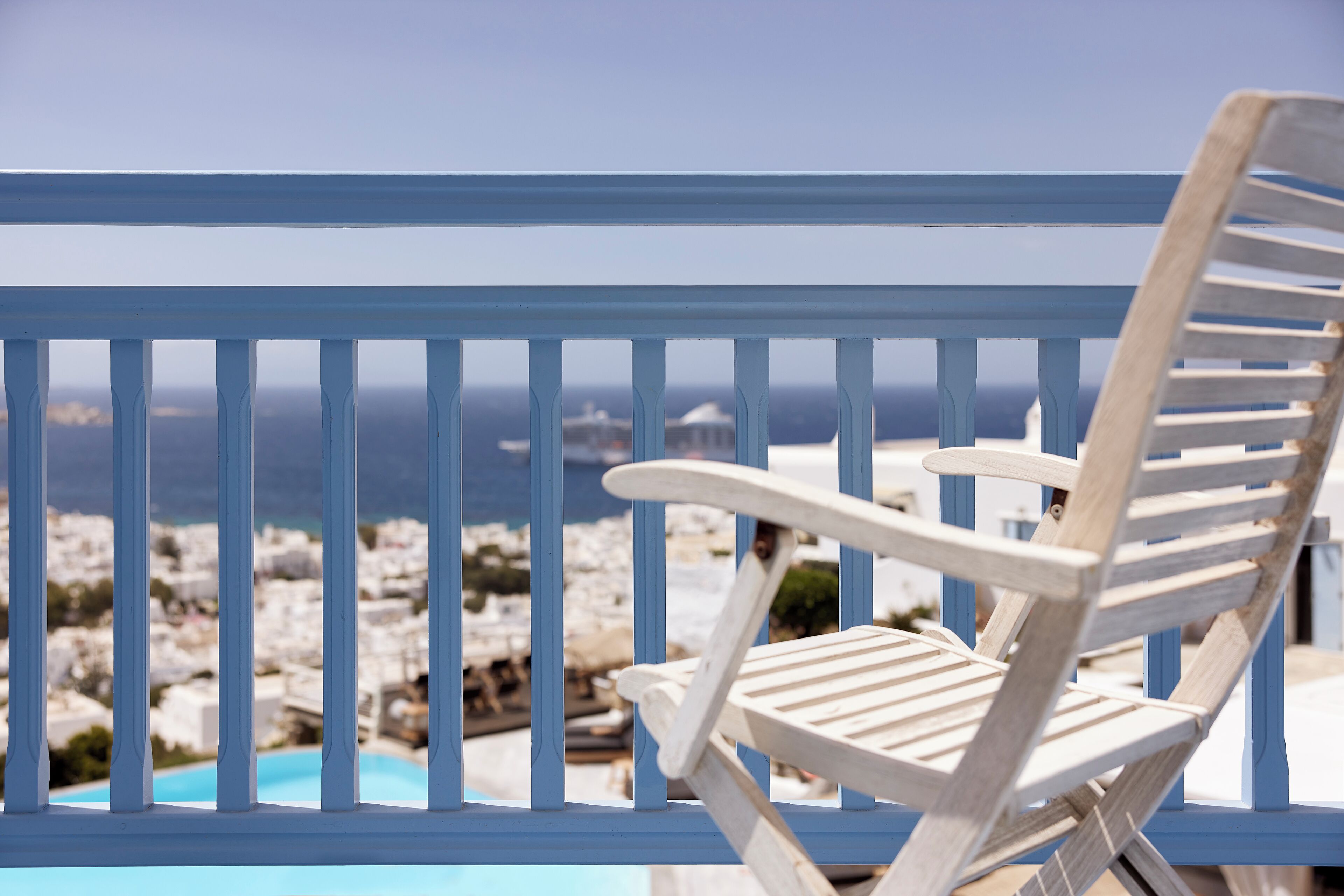 A white wooden chair with a view of a coastal town and a clear sky.