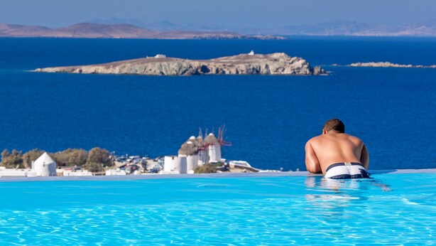 A man sitting in a swimming pool with a view of a coastal town and a distant island.