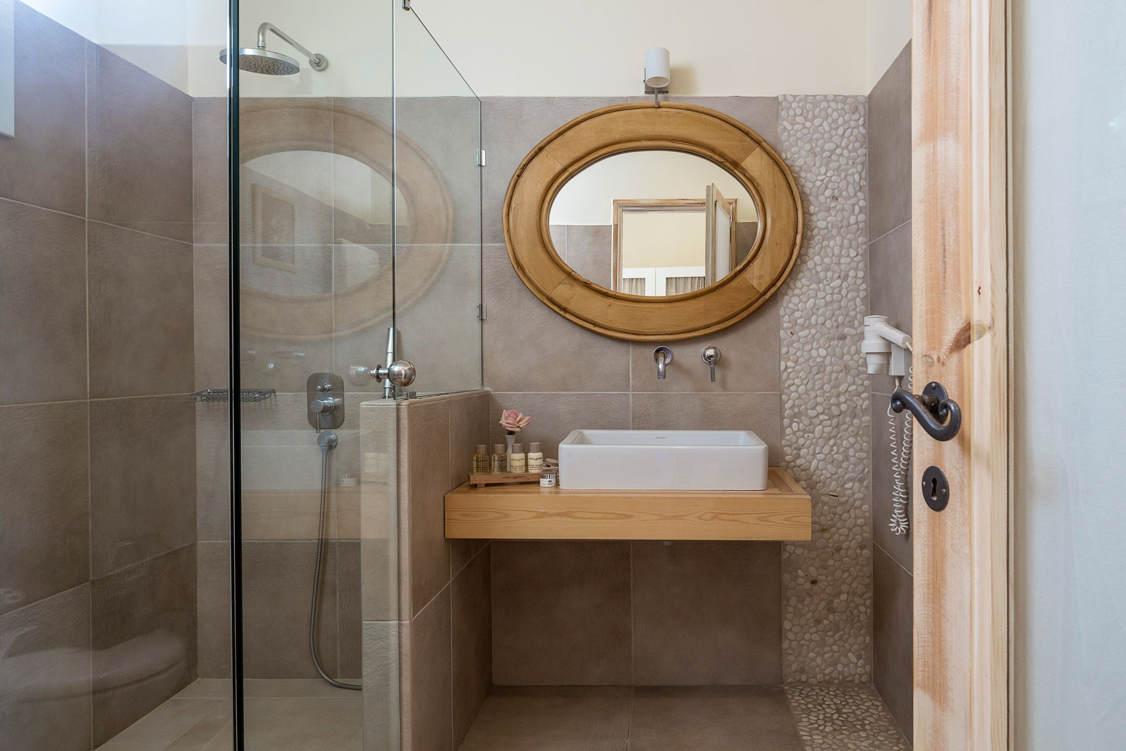 A modern bathroom with a glass-enclosed shower, a wooden vanity with a sink, and a round mirror.