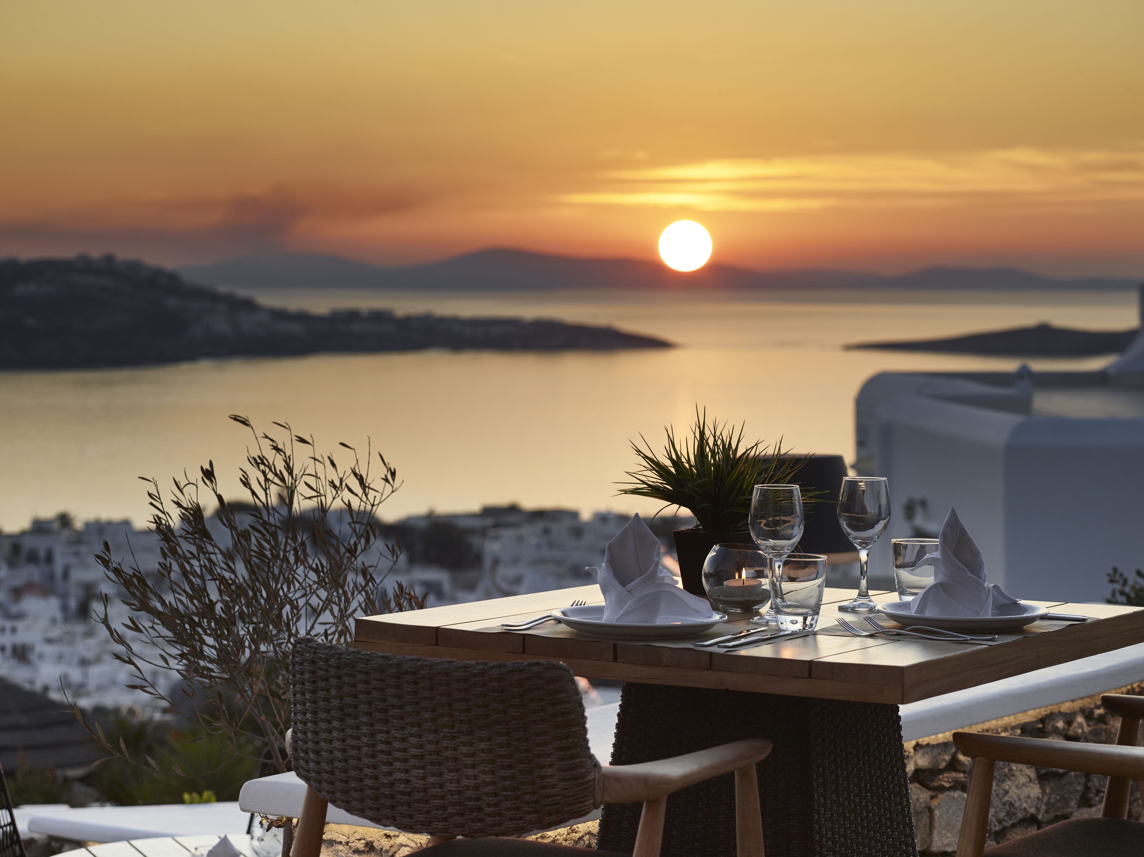 A table set for two with a view of the sunset over water.