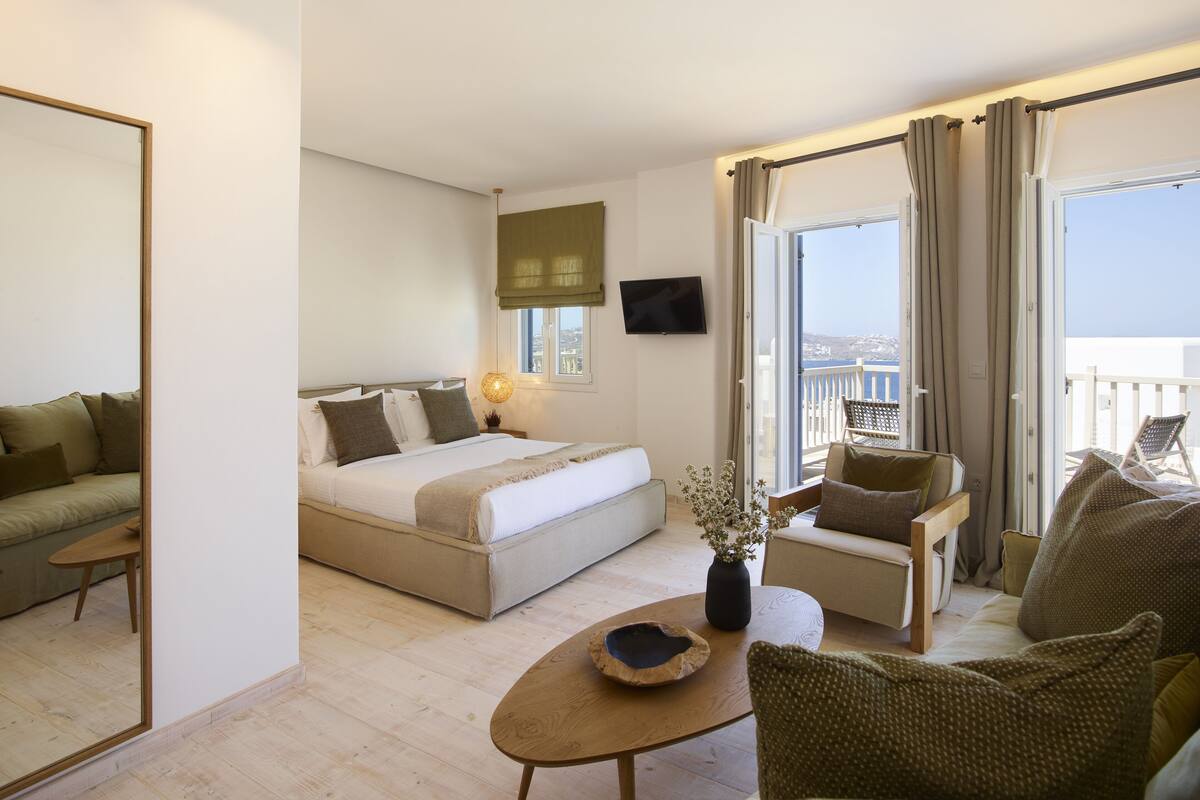 Een moderne hotelkamer met een bed, een bank, een tafeltje en een balkon met uitzicht.