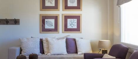 Un salon comprenant un canapé, deux fauteuils, une table basse et quatre œuvres d’art représentant des feuilles, encadrées et accrochées au mur.