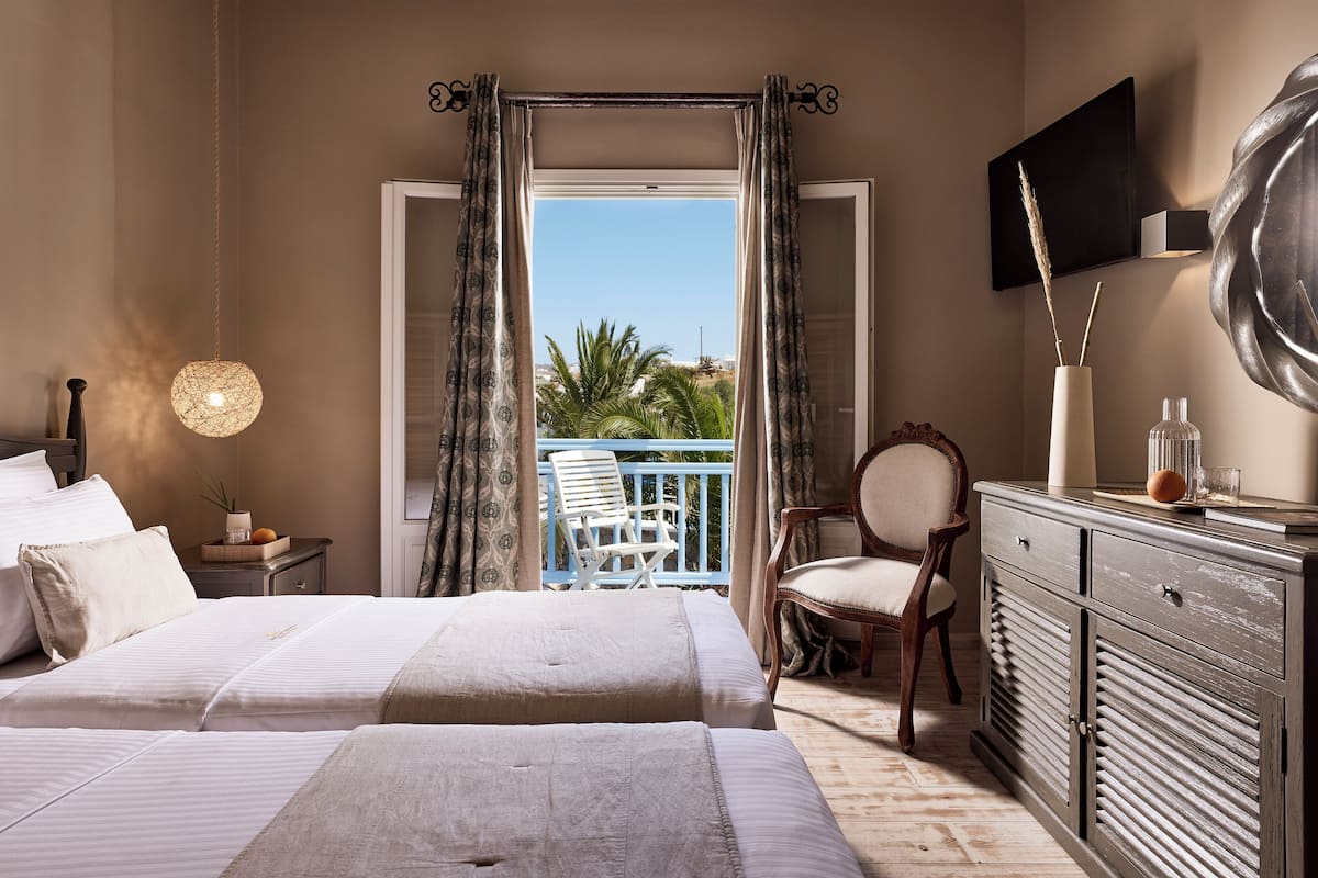 Een slaapkamer met twee bedden, een kaptafel, een stoel, een televisie en een balkon met uitzicht op palmbomen.