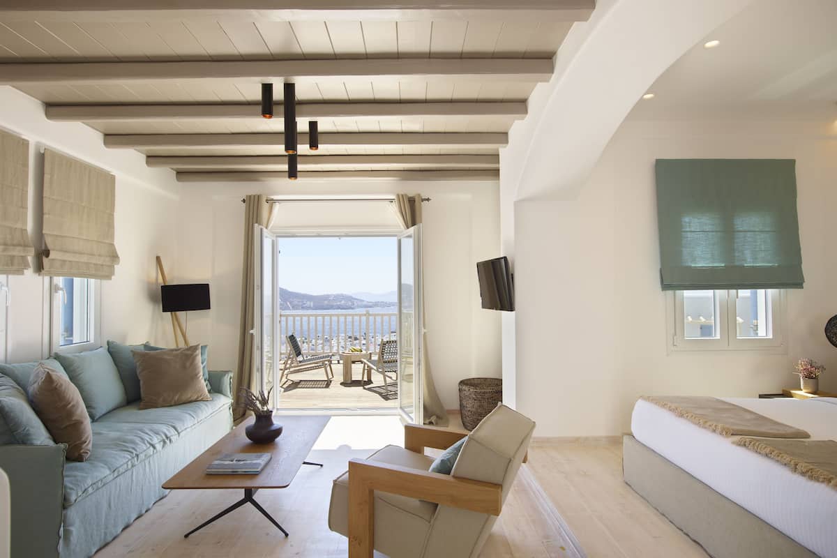 Een moderne woonkamer met een bank, fauteuil en salontafel. Er is een balkon met uitzicht op zee.